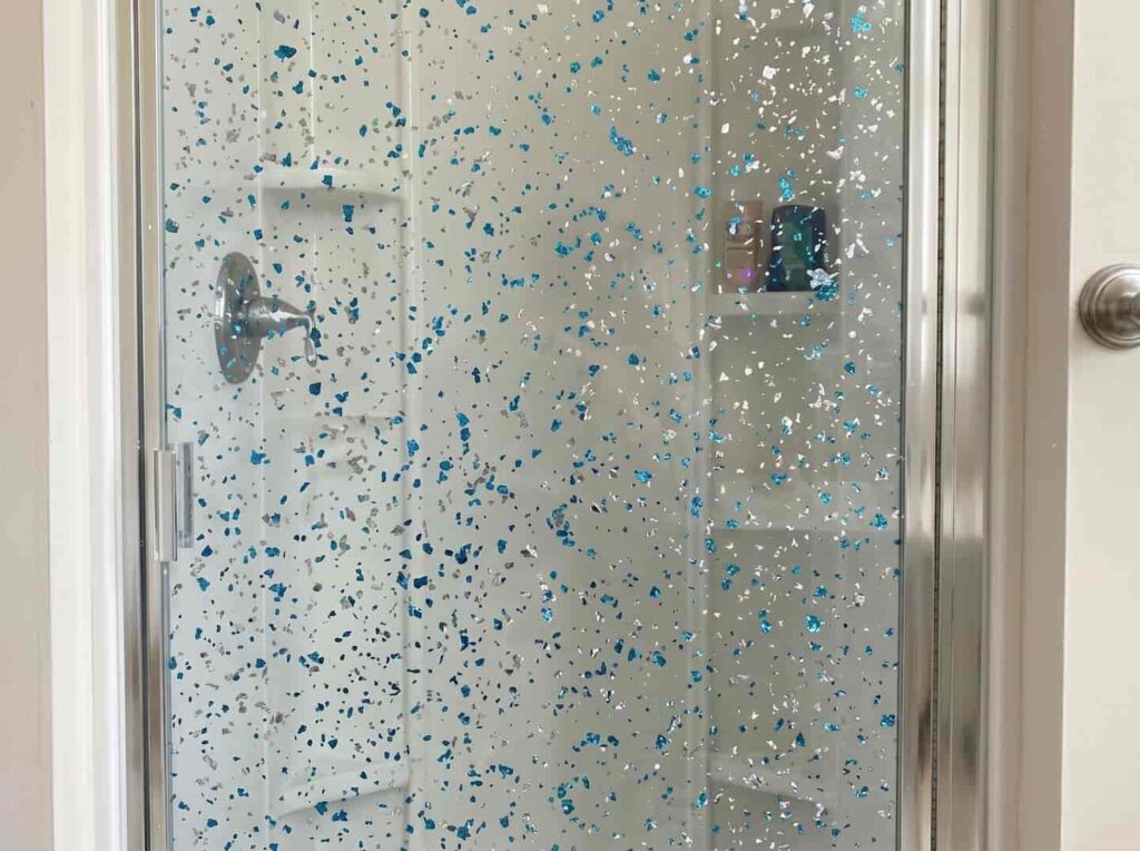 Transparent acrylic sheet featuring embedded blue and silver flakes, applied as a custom shower enclosure for luxury bathroom projects.