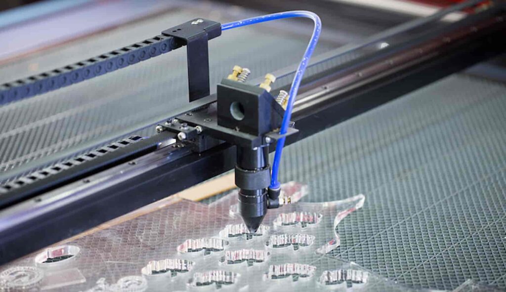 Top-down view of a laser engraver detailing complex patterns on a clear plexiglass material.